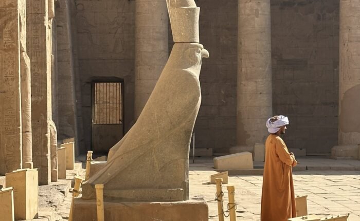 The granite Horus falcon statue in the courtyard of Edfu Temple, with a temple guard standing in front