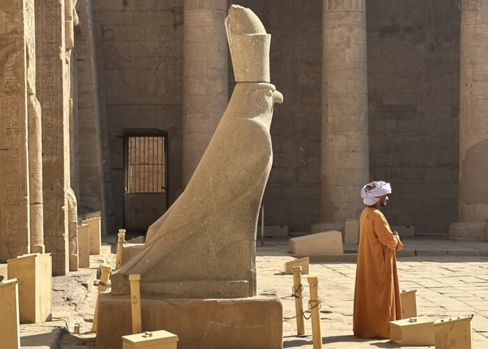 The granite Horus falcon statue in the courtyard of Edfu Temple, with a temple guard standing in front